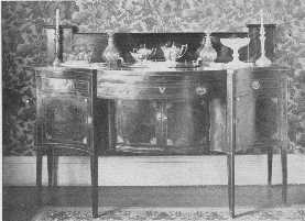 A fine old Hepplewhite sideboard, with old glass and
 silver, but the modern wallpaper is not in harmony.