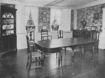The warm tones of a brown Chinese wallpaper are
 attractive with the mahogany furniture, and the pattern is prevented
from becoming monotonous by the strong rectangular lines of the ivory
woodwork which frames it. The corner cupboard and the exceptionally fine
dining-table and the variety of chairs are interesting.
