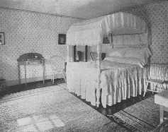 This bed-room is a good example of a simple Colonial
bed-room, and the rag rugs are in keeping with it. The repeat design of
the wallpaper ties the room into a unified whole.
